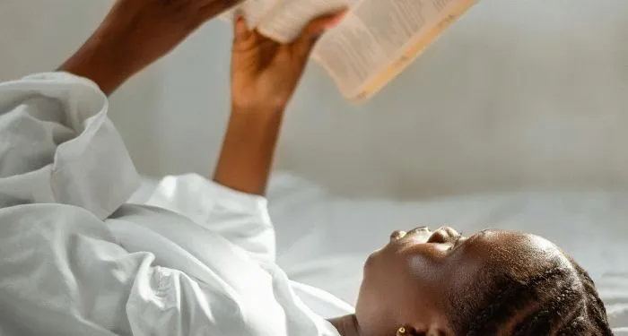 brown skinned Black woman laying down and reading a book